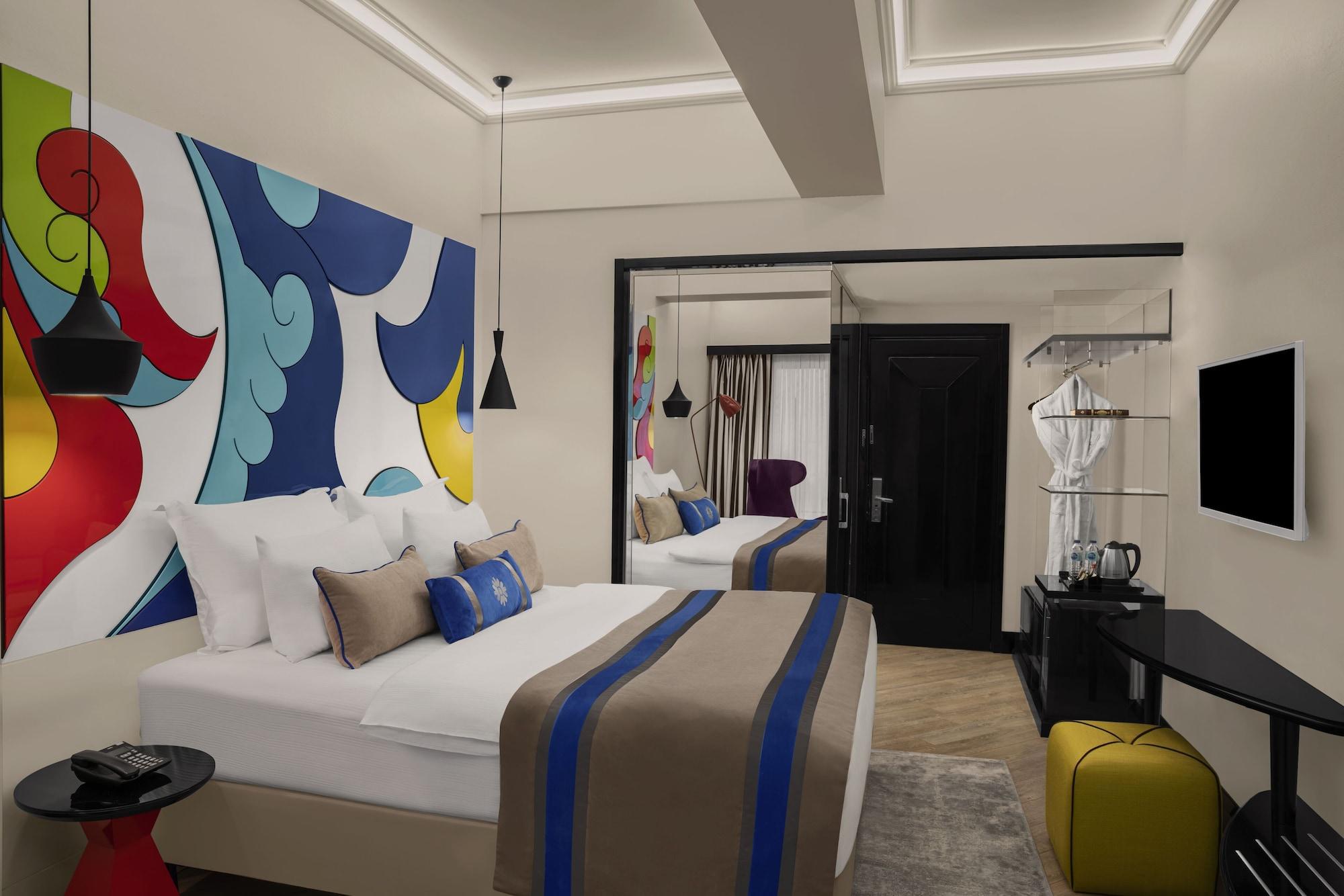 Sura Hagia Sophia Hotel Истанбул Екстериор снимка The photo shows a stylish hotel room featuring a modern design. There are two beds with white linens and decorative pillows in neutral colors, along with a distinctive blue accent. The room has a colorful mural on one wall with abstract shapes in vib