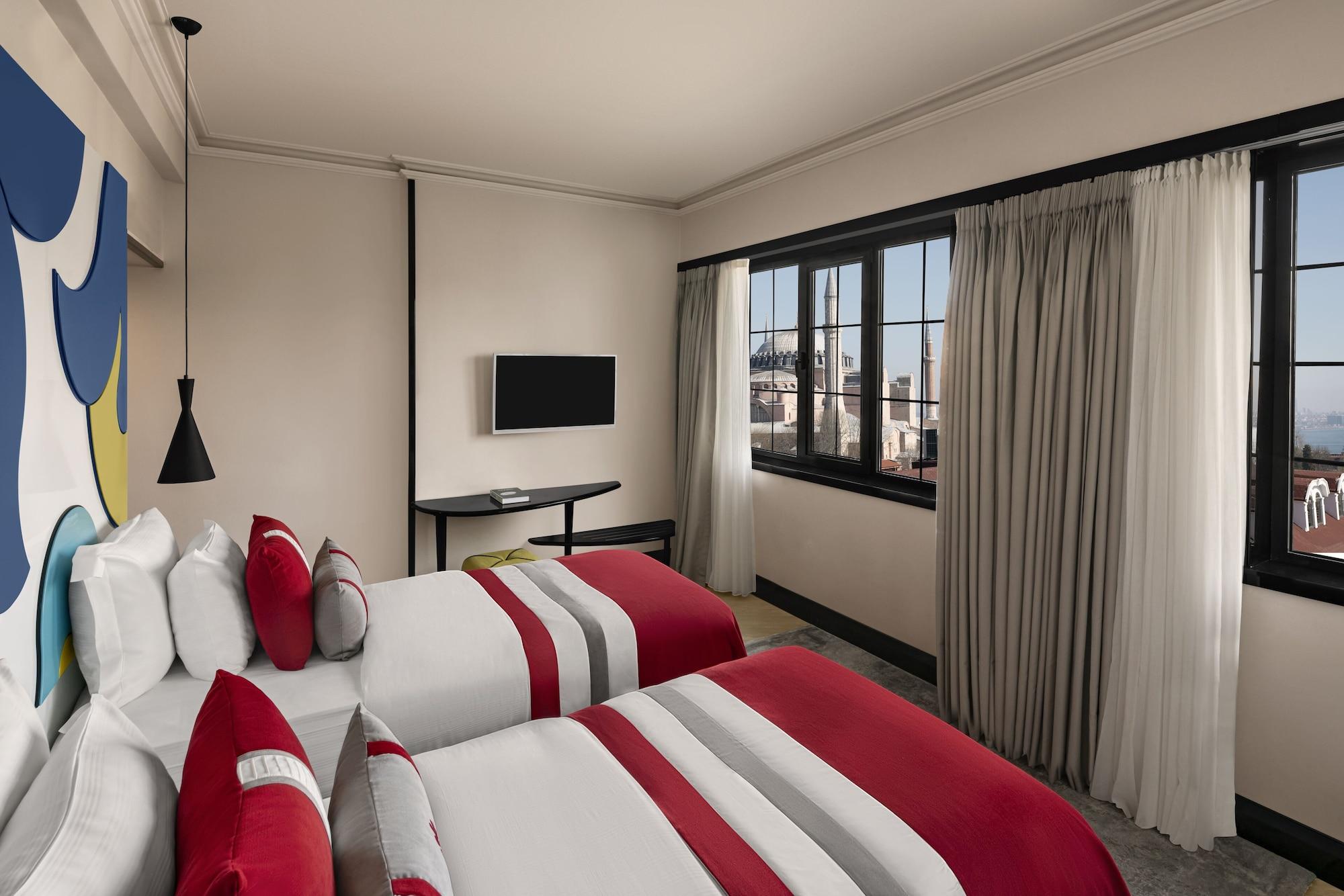 Sura Hagia Sophia Hotel Истанбул Екстериор снимка The photo shows a modern hotel room featuring two beds with red and white striped bedspreads. The walls are painted in a neutral color, and there are two windows with light-colored curtains that allow natural light to brighten the space. A small tabl
