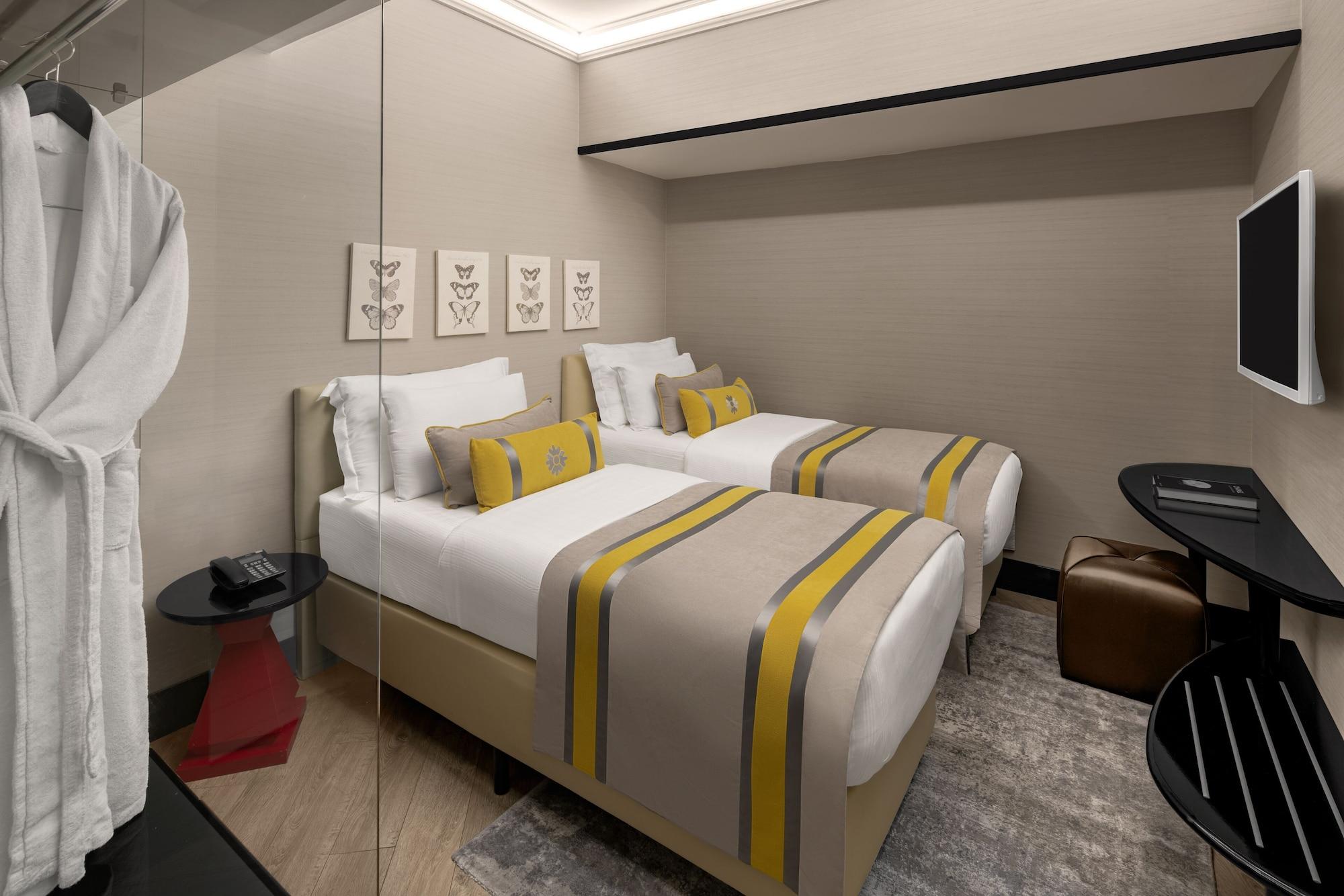 Sura Hagia Sophia Hotel Истанбул Екстериор снимка The photo shows a modern hotel room featuring two twin beds with white linens and decorative throw pillows in yellow. The beds have a simple, contemporary design with beige headboards. Behind the beds, there are framed artworks arranged on the wall. 