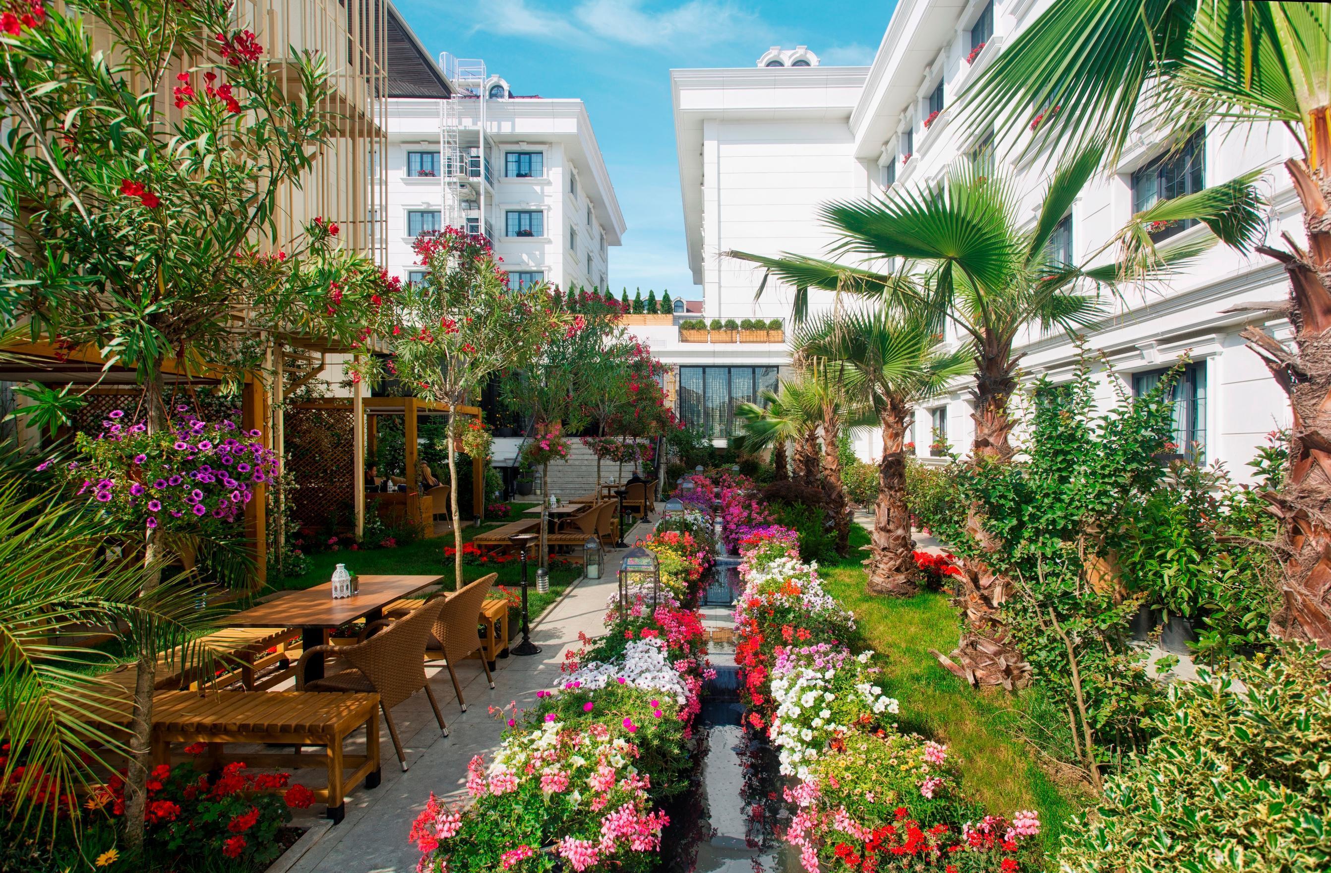 Sura Hagia Sophia Hotel Истанбул Екстериор снимка The photo depicts a beautiful garden area, featuring a variety of colorful flowers and lush greenery. There are pathways lined with vibrant blooms, creating a picturesque landscape. To one side, there are wooden seating arrangements, suggesting a spa