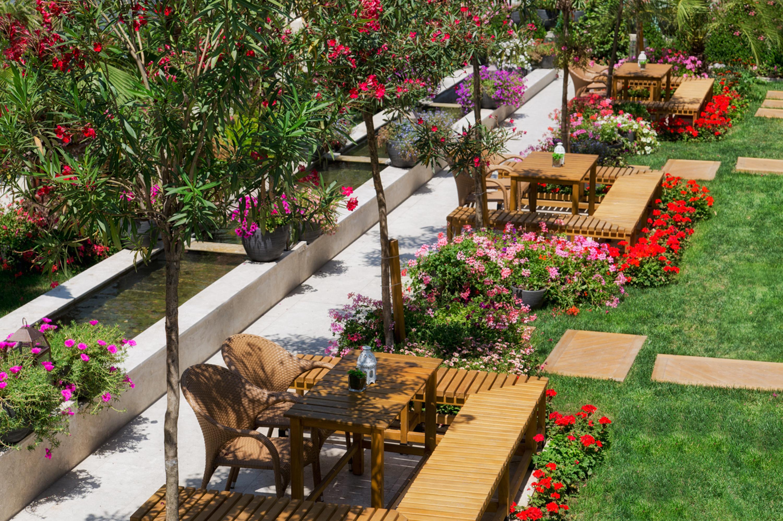 Sura Hagia Sophia Hotel Истанбул Екстериор снимка The photo shows a beautifully landscaped garden area featuring several wooden tables and chairs arranged along pathways. These seating areas are surrounded by vibrant flower beds filled with colorful blooms, including pinks and reds. There are small 