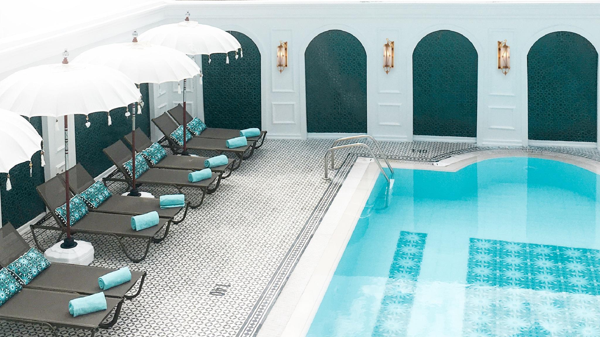 Sura Hagia Sophia Hotel Истанбул Екстериор снимка The photo depicts an elegant indoor swimming pool area. The pool has a light blue hue and features a decorative tile pattern along the bottom. Surrounding the pool, there are several lounge chairs with turquoise cushions and large white umbrellas for