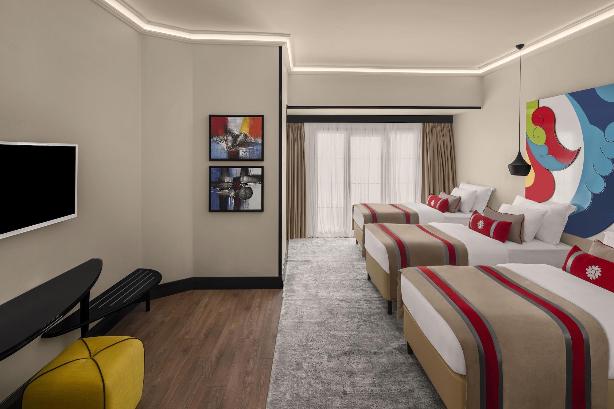 Sura Hagia Sophia Hotel Истанбул Екстериор снимка The photo depicts a modern hotel room featuring a light-colored interior. There are three beds with stylish bed linens that include bold red and neutral tones. A large piece of abstract art adorns one wall, and there are two framed pictures on anothe