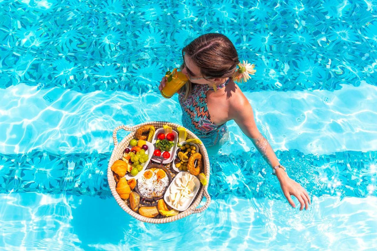 Sura Hagia Sophia Hotel Истанбул Екстериор снимка The photo shows a woman standing in a swimming pool, partially submerged in the water. She is holding a large, round basket filled with a variety of food items, including fruits and pastries. The scene is vibrant and tropical, with the woman wearing 